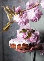 uma mulher decora uma caseiro Páscoa bolo com Rosa sakura flores, primavera Flor foto