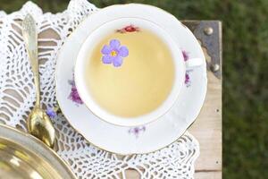 porcelana copo com chá e flor flutua dentro chá, vintage ainda vida, topo Visão foto