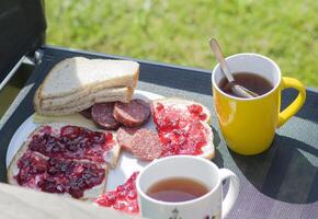 café da manhã dentro a jardim em uma cadeira dois sanduíches com linguiça e manteiga geléia foto