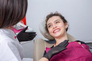 fechar-se do fêmea paciente mostrando dela lindo branco dentes enquanto tendo tratamento às dental clínica, dentista mãos dentro borracha luvas segurando dental Ferramentas foto