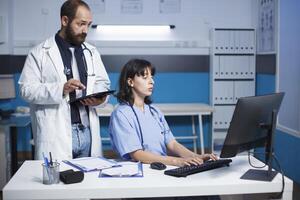 masculino médico e fêmea enfermeira discutir com digital dispositivos mostrando raios X dentro uma clínica escritório. azul esfoliantes, laboratório casacos, estetoscópio, e uma vídeo conferência com o negócio parceiros. foto