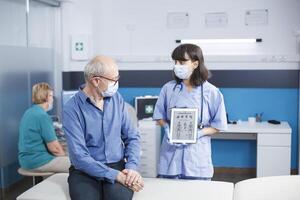 fêmea médico mostra idosos paciente vestindo face mascarar uma tábua exibindo humano esqueleto. digital gadget é mantido de enfermeira quem é dando uma médico diagnóstico para Senior aposentado cara. foto