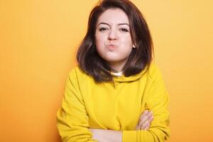 confiante beleza modelo com morena cabelo faz uma beijinho face em Câmera enquanto posando despreocupado dentro a estúdio. retrato do jovem fêmea adulto com braços cruzado fazer uma pateta face. foto