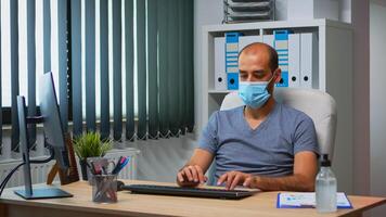 homem de negocios com médico proteção face mascarar digitando em computador dentro escritório sala. empreendedor dentro Novo normal pessoal local de trabalho corporativo escrevendo em pc teclado olhando às Área de Trabalho foto