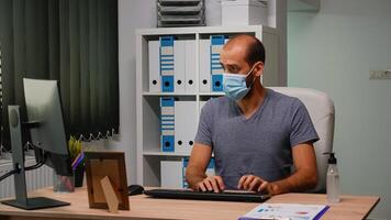 empreendedor com mascarar digitando em computador sentado dentro Novo normal ambiente de trabalho. trabalhador autonomo trabalhando dentro moderno escritório área de trabalho limpeza mãos usando higienizar álcool gel contra corona vírus foto