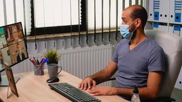 o negócio homem sentado dentro frente do computador dentro Novo normal escritório tendo vídeo ligar vestindo proteção mascarar. trabalhador autonomo discutindo conversando durante virtual conferência, reunião, usando Internet tecnologia. foto