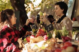 mulher pequeno o negócio proprietário falando para velho cliente e vendendo fresco localmente crescido legumes às agricultores mercado. fornecedor ajudando cliente para escolher legumes, explicando saúde benefícios do orgânico Comida. foto