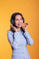 alegre filipino mulher ouvindo música e dançando, desfrutando livre Tempo dentro estúdio sobre amarelo fundo. atraente modelo vestindo fones de ouvido mostrando engraçado dança movimentos. entretenimento conceito foto