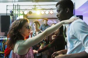 jovem casal dentro amor dançando enquanto festa e relaxante dentro Boate. caucasiano namorada e africano americano namorado fazer apaixonado movimentos em pista de dança enquanto balada foto