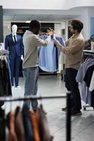 africano americano homem selecionando formal equipamento e Perguntando roupas loja assistente para conselho. compras Shopping boutique empregado e cliente discutindo camisa e gravata estilo Combine foto
