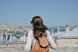 uma jovem viajante com uma mochila em dela costas parece às a panorama a partir de a suleymaniye mesquita em uma ensolarado dia dentro Istambul. foto