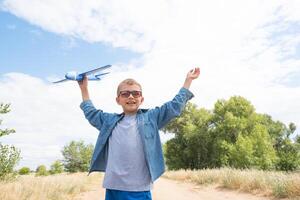 feliz criança jogando com uma brinquedo avião contra uma azul céu dentro a aberto campo foto