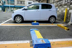 Osaka cidade, Japão, 2023 - fechar-se a metal prato debaixo a carro para para trava a rodas e carro com pequeno carro estacionado dentro pago estacionamento muito. foto