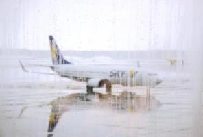 Hokkaido, Japão, 2023 - borrado pingos de chuva em terminal do aeroporto janelas com a céu CIA aérea avião estacionado em molhado pista e nebuloso clima fundo. foto