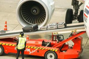 Bangkok cidade, tailândia, 2023 - fechar-se funcionários do tailandês ar Ásia CIA aérea usando Bagagem carregador carrinho Carregando bagagem para a avião. foto