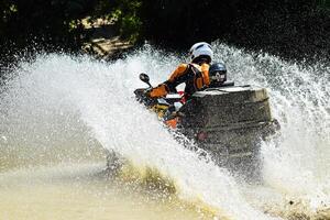 a homem em a atv cruzes uma fluxo. turista anda em em uma pelo país terreno foto