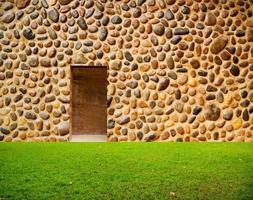 parede de pedra com porta e piso de grama na frente foto