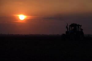 trator aração arado a campo em uma fundo pôr do sol. trator silhueta em pôr do sol fundo foto