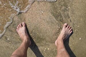 pernas homens em a mar areia perto mar onda foto