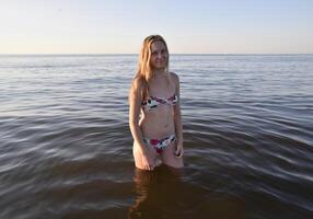 loiro menina dentro uma bikini em pé dentro a mar água. lindo jovem mulher dentro uma colorida bikini em mar fundo foto