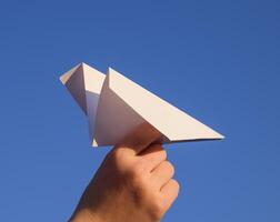 branco papel avião dentro mão contra a céu. uma símbolo do liberdade em a Internet foto