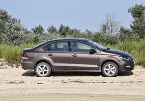 Volkswagen pólo carro em a de praia dentro a areia contra uma fundo do vegetação. foto