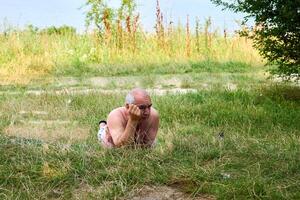 a idosos homem é em repouso em uma Relva dentro uma gramado perto uma verão rio foto