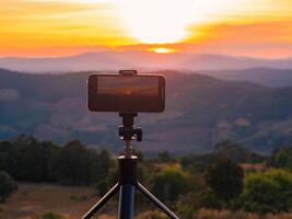 uma Smartphone é gravação a Sol configuração sobre uma montanha faixa. foto