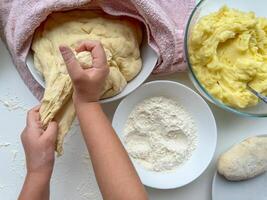 a mãos do criança amassar a massa para fazer tortas em branco mesa, topo visualizar. foto