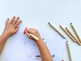 pequeno criança desenha com colori lápis em papel em branco mesa. foto