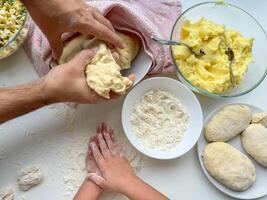 a mãos do criança e pai amassar a massa para fazer tortas em branco mesa, topo visualizar. foto