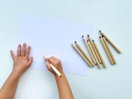 pequeno criança desenha com colori lápis em papel em branco mesa. foto