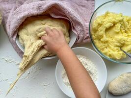 a mãos do criança amassar a massa para fazer tortas em branco mesa, topo visualizar. foto