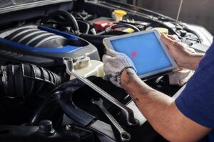 a mecânico Verificações a motor usando tábua computador tecnologia. completo com chave inglesa ferramenta auto mecânico trabalhando dentro a garagem. reparar serviço. foto