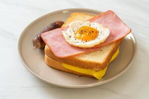 pão torrado queijo com cobertura de presunto e ovo frito com linguiça de porco foto