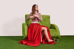 jovem mulher pentear dela grandes em linha reta cabelo com uma pente enquanto sentado em a sofá dentro a estúdio foto
