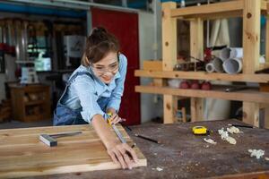 jovem mulher é Treinamento para estar uma carpinteiro dentro oficina. carpinteiro trabalhando com equipamento em de madeira mesa. mulher trabalho dentro uma carpintaria fazer compras. foto