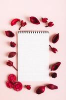 caderno para escrevendo dentro uma quadro, Armação do seco vermelho flores em uma Rosa fundo topo e vertical Visão foto