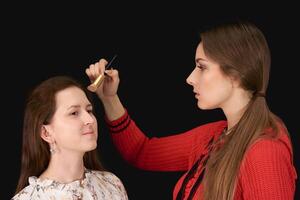 fêmea Maquiagem artista aplica-se cosméticos para modelo em Sombrio fundo foto