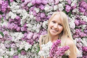 feliz jovem mulher com uma ramalhete em uma fundo do florescendo lilases foto