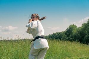 Adolescência menina Treinamento karatê kata ao ar livre, prepara para uro mawashi geri gancho pontapé foto