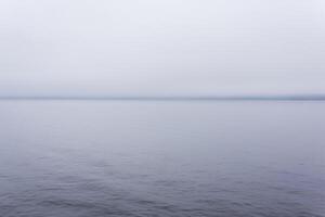 frio corpo do água com uma distante costa escondido de névoa foto