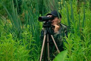 masculino ornitólogo faz observações dentro a selvagem com uma manchando escopo foto