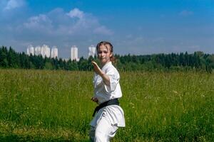 Adolescência menina Treinamento karatê kata ao ar livre, executa soto uke ou lado de fora quadra foto