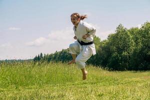 adolescente menina Treinamento karatê kata ao ar livre, executa uma pontapé dentro uma saltar foto