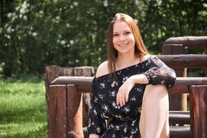 sorridente menina sentado em uma parque Banco dentro uma livre pose foto