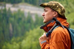 homem geólogo com uma mochila e uma geológico martelo dentro mão contra a pano de fundo do uma arborizado montanha panorama foto