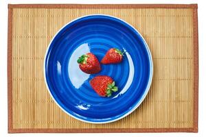 três morangos em uma azul prato em uma bengala Lugar, colocar esteira foto