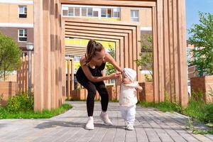 mãe e criança pequena filha andar dentro a cidade pátio, criança aprende para andar foto