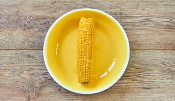 amarelo espiga do fervido milho em uma amarelo prato em uma de madeira de mesa foto